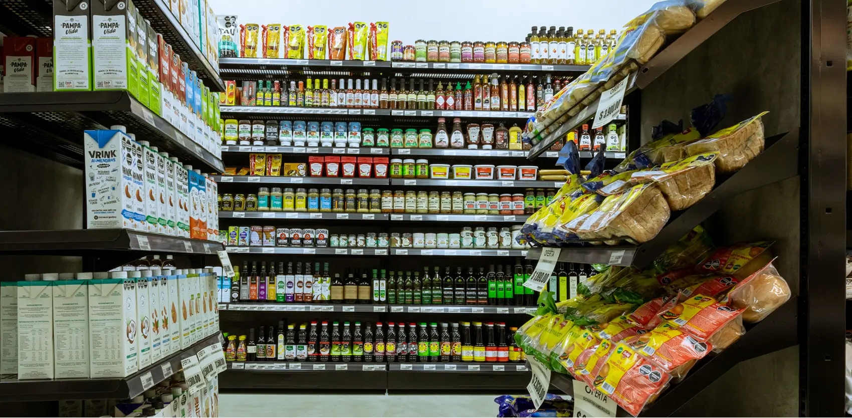 Pasillo de supermercado con góndolas Wire exhibiendo productos de compra rápida como snacks, bebidas y alimentos en el inicio del corredor