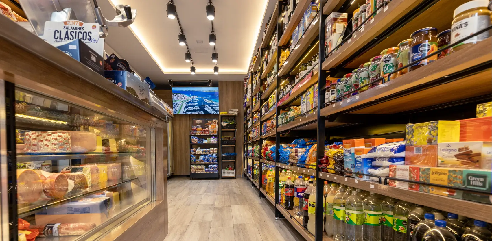 Tienda de proximidad con góndolas metálicas y heladera exhibiendo productos organizados en pasillo comercial